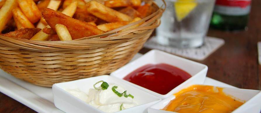 pomfrit serviran u pletenoj činiji pored koje su sosvevi za umakanje